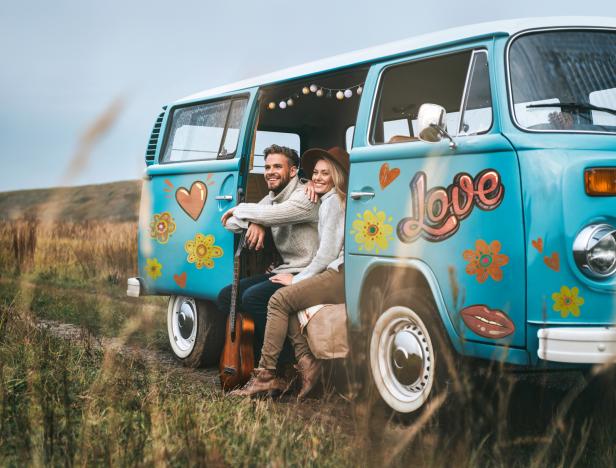 Ein Paar sitzt mit einer Gitarre in einem blau bemalten VW-Bus mit dem Schriftzug „Love“.