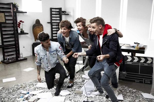 Die Band One Direction posiert auf einem Haufen Papierschnitzel vor einer Filmklappe.