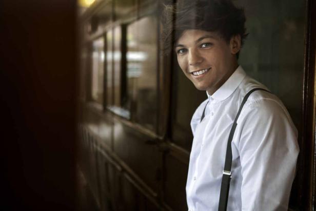 Louis Tomlinson lächelt in einem weißen Hemd mit Hosenträgern.