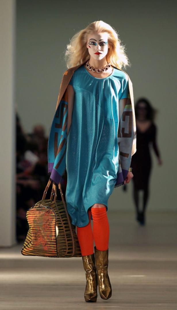 Eine Frau mit auffälligem Make-up läuft mit einer Tasche über den Laufsteg.