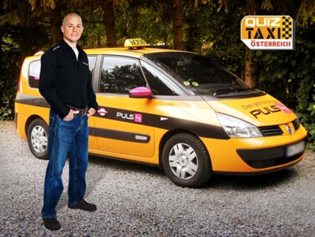 Ein Mann steht vor einem gelben „Quiz Taxi Österreich“-Taxi.