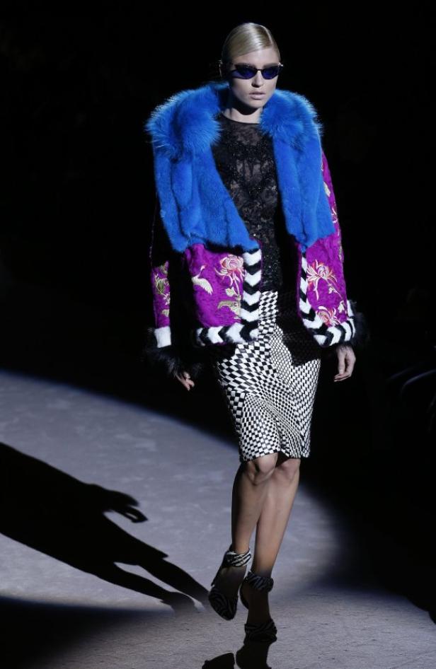 Ein Model präsentiert eine Jacke mit blauem Pelzkragen und einen schwarz-weiß karierten Rock.