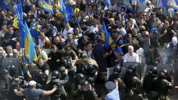 Eine Menschenmenge demonstriert mit ukrainischen Flaggen vor einer Reihe von Polizisten mit Schutzschilden.
