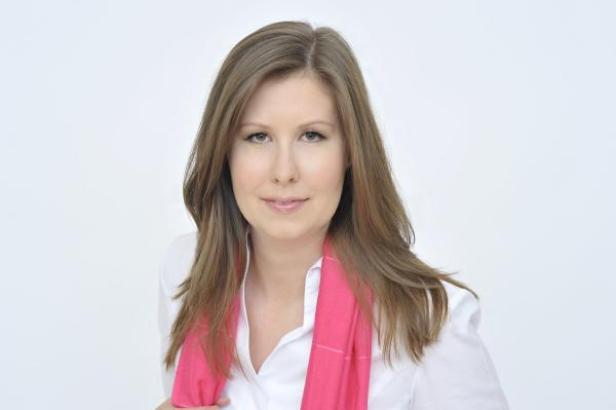 Eine Frau mit langen braunen Haaren und einem pinkfarbenen Schal lächelt.