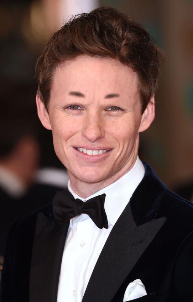 Eddie Redmayne lächelt in einem schwarzen Smoking.