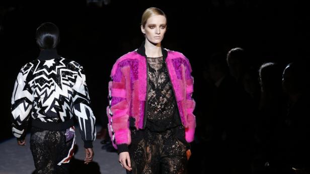 Eine Frau auf dem Laufsteg trägt eine pinkfarbene Jacke über einem schwarzen Spitzenoberteil.