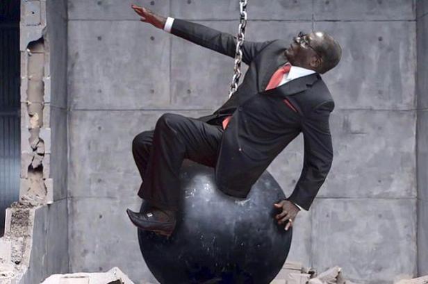 Ein Mann im Anzug reitet auf einer Abrissbirne vor einer Betonwand.