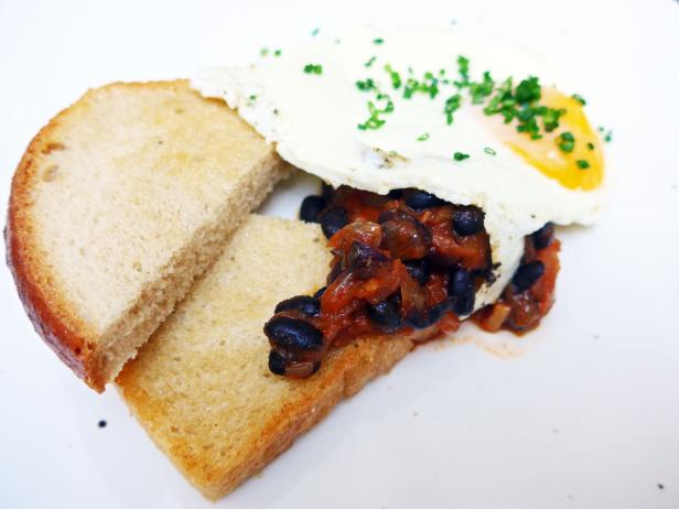 Ein Teller mit Toast, schwarzen Bohnen in Tomatensauce und einem Spiegelei mit Schnittlauch.