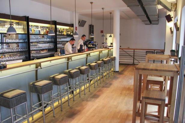 Blick in eine Bar mit Hockern an der Theke und zwei Barkeepern.