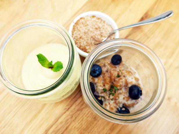 Drei Gläser mit Dessert, darunter Mousse, Müsli und Blaubeeren, auf einem Holztisch.