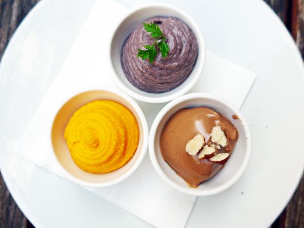 Drei Schälchen mit Dips in Gelb, Lila und Braun stehen auf einem Teller.