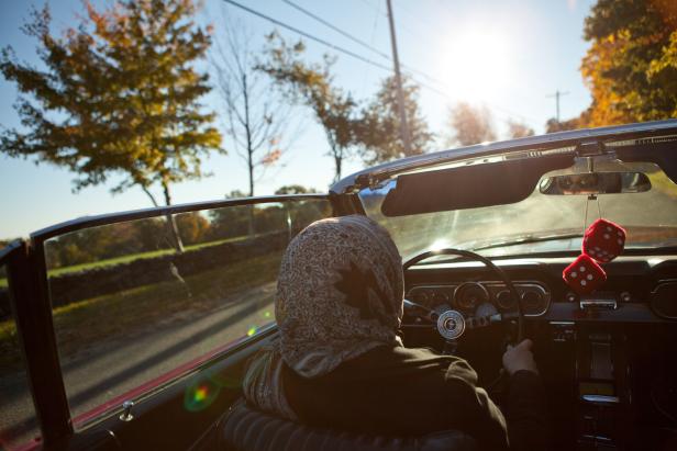 Eine Person fährt einen roten Oldtimer-Cabriolet auf einer Landstraße.