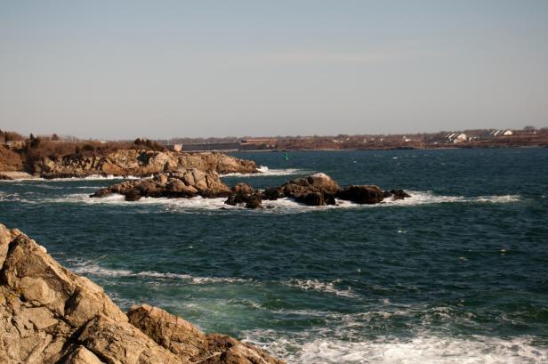 Eine felsige Küstenlinie mit Brandung an einem sonnigen Tag.