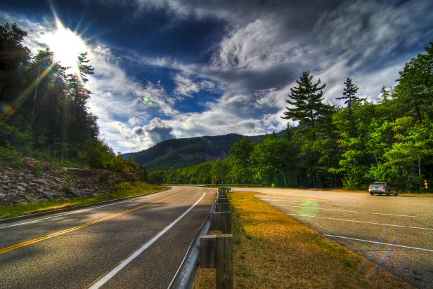 Eine kurvenreiche Straße führt durch eine grüne Waldlandschaft mit bewölktem Himmel.