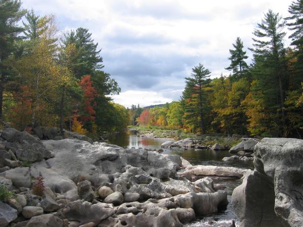 Ein Fluss fließt durch eine felsige Landschaft mit herbstlichen Bäumen.