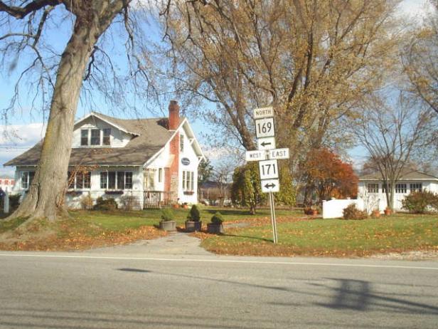 Ein weißes Haus steht an einer Straßenecke mit Wegweisern nach Norden (169) und Westen/Osten (171).