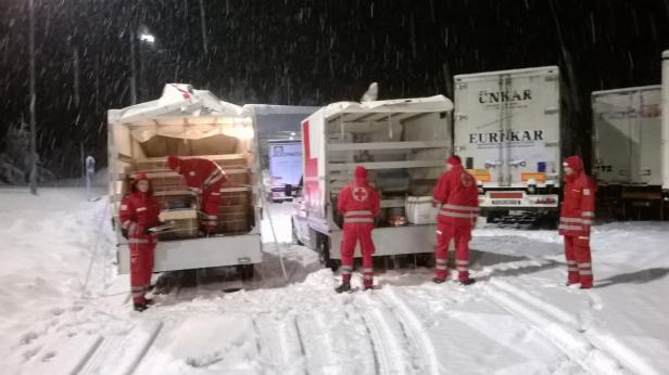 Rettungskräfte des Roten Kreuzes entladen Hilfsgüter aus Lastwagen im Schnee.