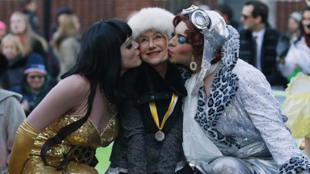 Helen Mirren wird von zwei Dragqueens auf die Wange geküsst.
