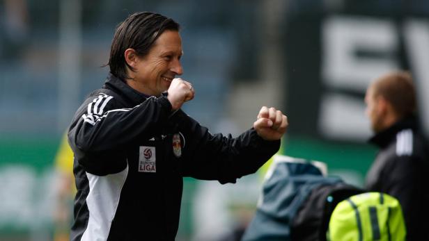 Ein Trainer jubelt mit geballten Fäusten auf dem Fußballplatz.