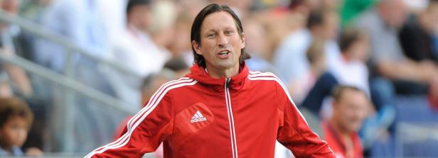 Ein Mann in einer roten Adidas-Jacke gestikuliert vor einer Zuschauermenge.