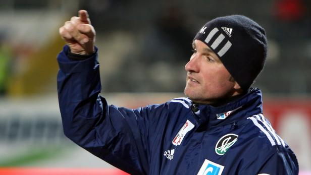 Ein Mann in Trainingskleidung und Mütze gestikuliert mit erhobenem Zeigefinger.