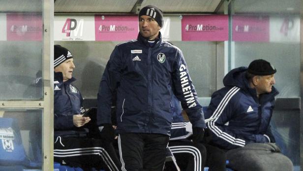 Ein Fußballtrainer steht vor der Auswechselbank, während seine Kollegen sitzen.