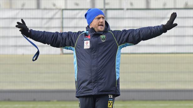 Ein Trainer mit blauer Mütze gestikuliert auf einem Fußballfeld.