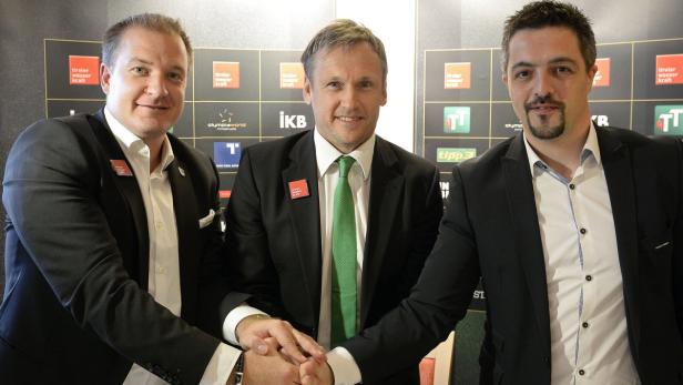 Drei Männer in Anzügen geben sich die Hände vor einer Wand mit Logos.