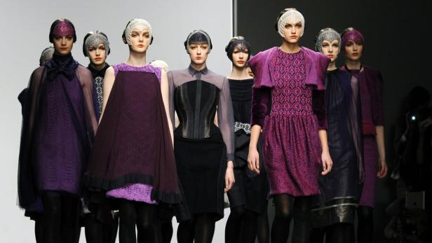 Models präsentieren violette und schwarze Kleider auf einem Laufsteg.