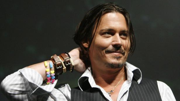 Johnny Depp lächelt mit der Hand am Hinterkopf.