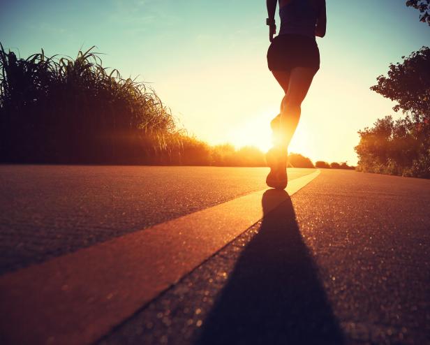 Eine junge, sportliche Frau läuft auf einem Küstenpfad in den Sonnenaufgang.