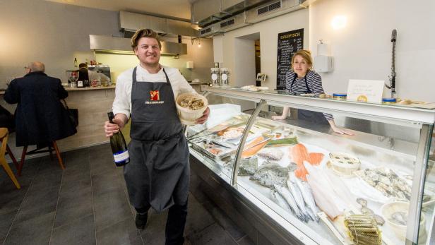 Ein Mann mit einer Flasche Wein und einem Korb steht in einem Fischgeschäft.