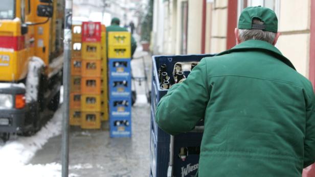 Ein Mann in grüner Jacke transportiert einen Kasten mit Bierflaschen.