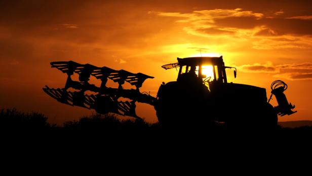 Die Silhouette eines Traktors mit Pflug vor einem orangefarbenen Sonnenuntergang.