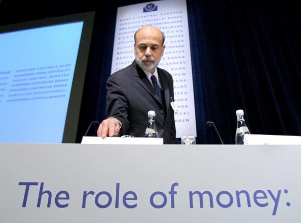 Ein Mann in einem Anzug steht hinter einem Podium mit der Aufschrift „The role of money“.