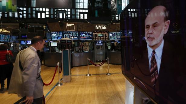 Blick in die New Yorker Börse mit einem Mann im Anzug und einem Fernsehbildschirm mit einer Person darauf.