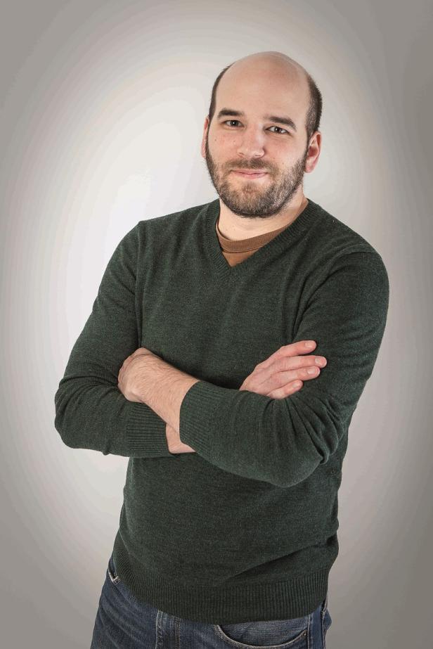 Ein Mann mit Bart und grünem Pullover steht mit verschränkten Armen da.