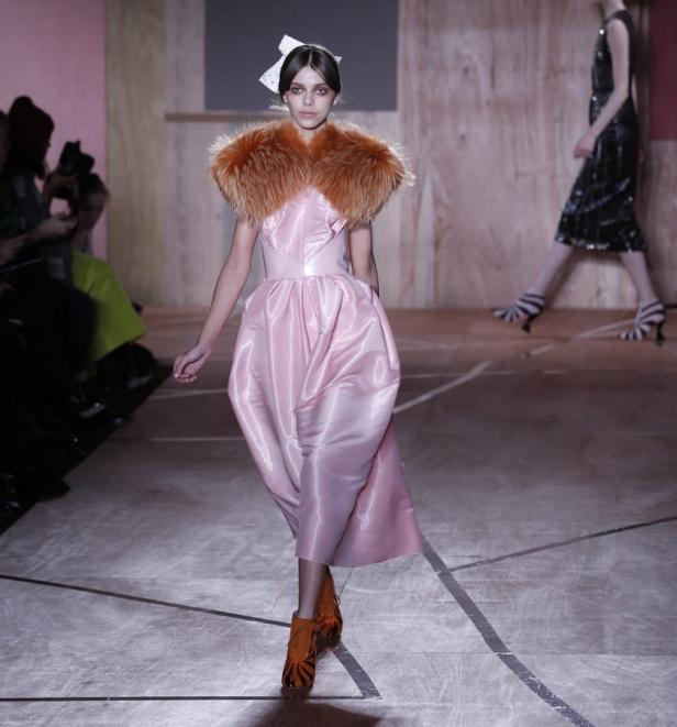 Ein Model in einem rosa Kleid mit Fellkragen auf einem Laufsteg.