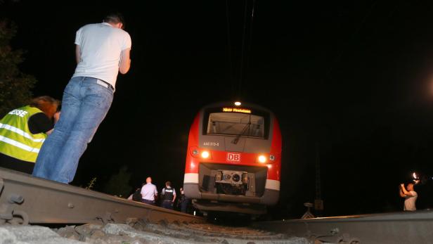 Ein roter Zug der Deutschen Bahn steht auf einem Gleis, umgeben von Personen.