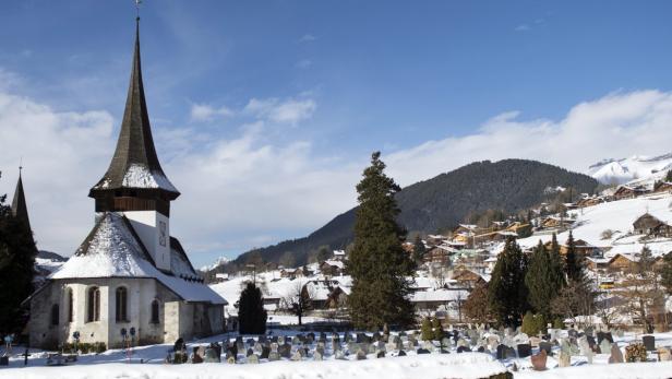 Eine verschneite Kirche mit Friedhof in einer Berglandschaft.
