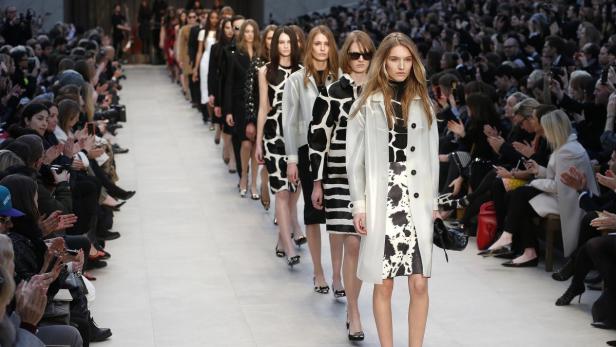 Models präsentieren eine Modenschau mit schwarz-weißen Designs vor einem applaudierenden Publikum.