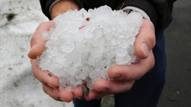 Schwere Hagelschäden in Tirol (Symbolfoto). Eine Person hält eine große Menge Hagel in ihren Händen.