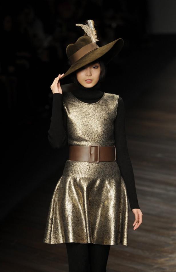 Eine Frau mit Hut und goldenem Kleid auf dem Laufsteg.