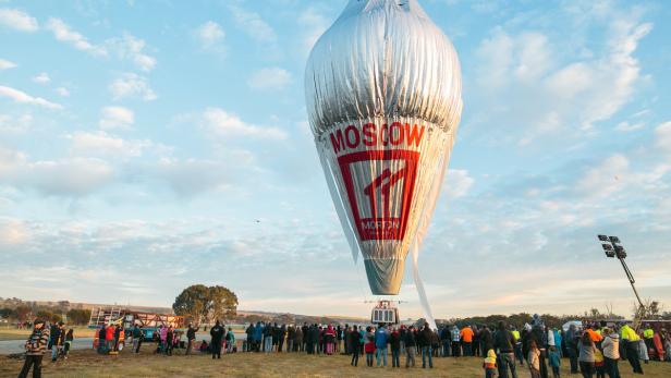 Ein silberner Heißluftballon mit der Aufschrift „Moscow“ wird von einer Menschenmenge beobachtet.