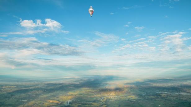 Ein Heißluftballon schwebt über einer grünen Landschaft unter blauem Himmel.