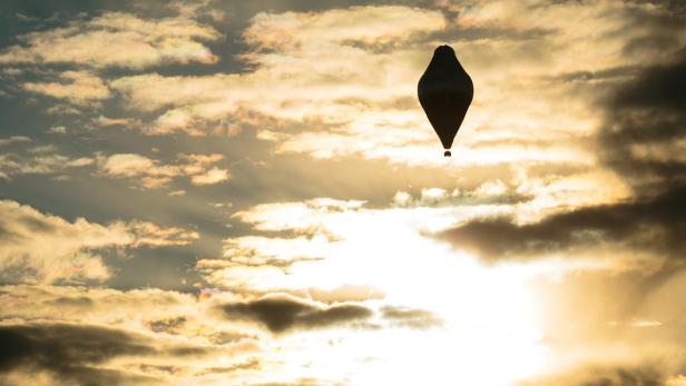 Ein Heißluftballon schwebt vor einem bewölkten Himmel im Gegenlicht.