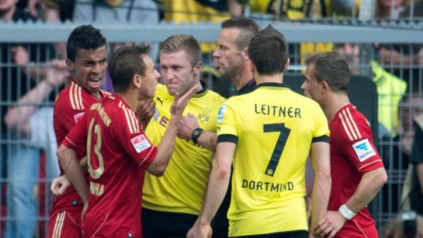 Fußballspieler in roten und gelben Trikots diskutieren mit einem Schiedsrichter.