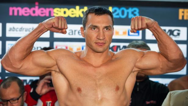Wladimir Klitschko spannt seine Muskeln vor einer Sponsorenwand an.