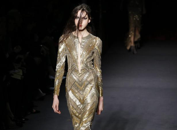 Ein Model präsentiert ein goldenes, paillettenbesetztes Kleid auf dem Laufsteg.