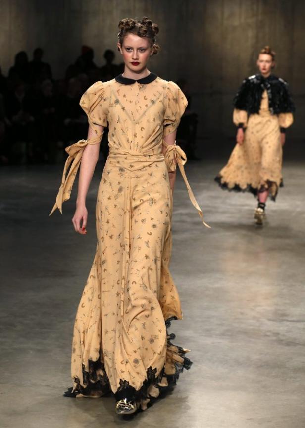 Eine Frau in einem langen, hellgelben Kleid mit schwarzen Akzenten auf einem Laufsteg.